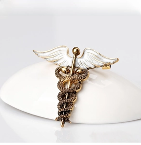 Detailed macro of golden Caduceus snake brooch with white enamel wings and relief texture