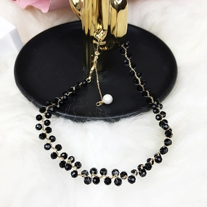 Elegant black beaded necklace with white pearl pendant and gold clasp on a black tray