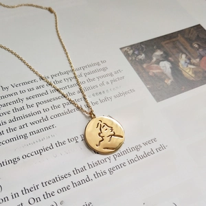 Artistic close-up of a gold face-shaped hollow pendant on a vintage art book page