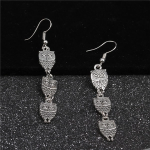Detailed macro view of triple owl pendant drop earrings in a vintage silver finish
