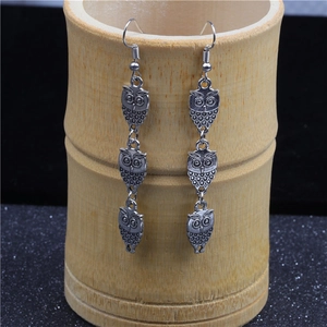Detail of vintage silver triple owl drop earrings hanging on a natural bamboo cup