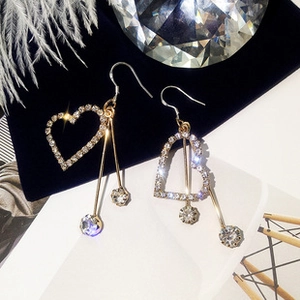 Detail of asymmetric gold tassel earrings featuring crystal hearts and long bars