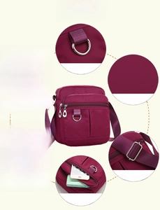 Detail view of purple nylon crossbody bag features multiple zippers and adjustable strap