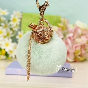 Détail d'un porte-clés pompon en fausse fourrure vert clair avec cloche dorée ciselée