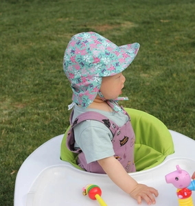 Detail of floral baby sun hat with wide brim, ear protection, and neck flap on grass