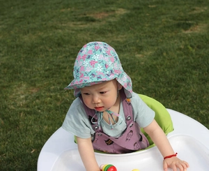 Detail of mint green baby sun hat with floral print and protective neck flap on grass