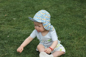 Close-up of baby sun hat with whale print and neck flap on outdoor green grass