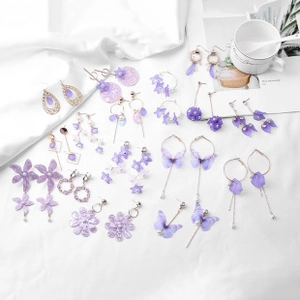 Flat lay of purple floral and butterfly earrings with rhinestones on white fabric