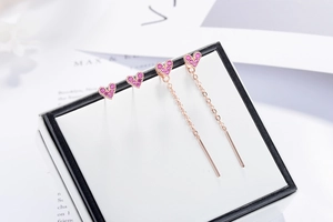 Detailed macro view of rose gold heart earrings with pink rhinestones on a gift box