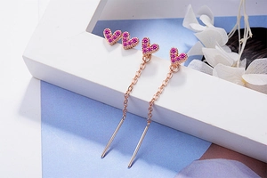 Detail showing rose gold heart earrings with pink zircons on elegant flower background