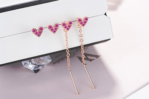 Macro detail of rose gold heart earrings with pink crystals and long chain tassels