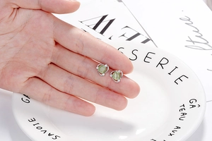 Macro shot of silver flower stud earrings with cat eye stone and zircons on a fingertip