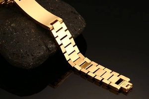 Detailed view of a gold-plated stainless steel watchband on a dark stone surface
