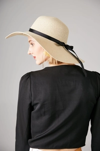 Detail of a beige wide brim straw sun hat with an elegant black grosgrain ribbon bow