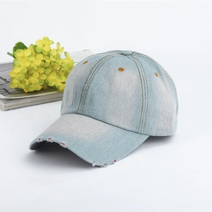 Detail of light blue washed denim baseball cap featuring distressed brim on white background