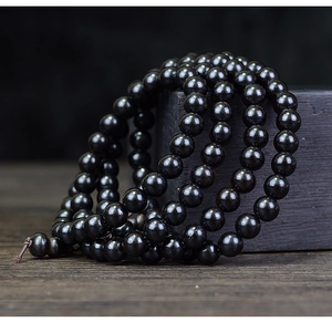 Detailed view of 108 black ebony wood prayer beads draped over a dark wooden block
