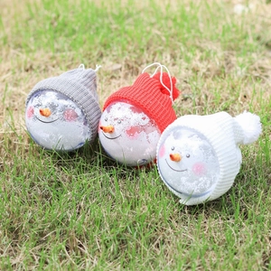 Three snowman Christmas ornaments with colorful hats on green grass outdoors