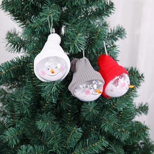 Three snowman clear ornaments with knit hats hanging on a festive Christmas tree detail