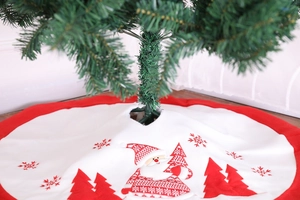Detail of red and white embroidered Christmas tree skirt with Santa and snowflake patterns