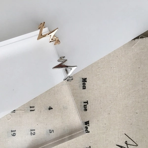 Detail shot of gold and silver heartbeat pulse wave rings on a white textured backdrop