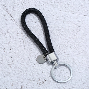 Close-up of black braided leather keychain with silver metal U-ring and circular tag