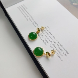 Detailed view of green agate stud earrings with gold plating on a fashion book background