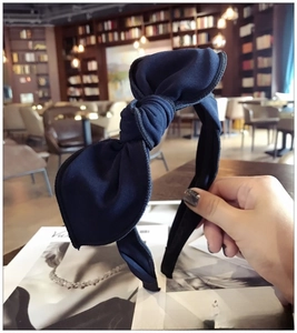 Close-up of navy blue fabric bow headband with visible woven texture held by hand