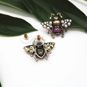 Detailed view of bee stud earrings with pearls and pink crystals on white background