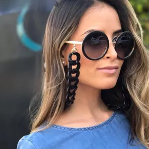 Detail of round black oversized sunglasses with gold temples and bold chunky chain strap