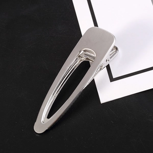 Detail view of a metallic silver duckbill hair clip with polished finish on black surface