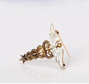 Detailed view of ancient gold caduceus brooch with white enamel wings and secure pin