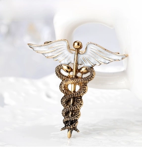 Macro shot of bronze Caduceus snake brooch with white enamel wings on a ceramic base