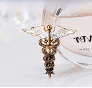 Macro view of a vintage gold Caduceus brooch with white enamel wings and snake texture