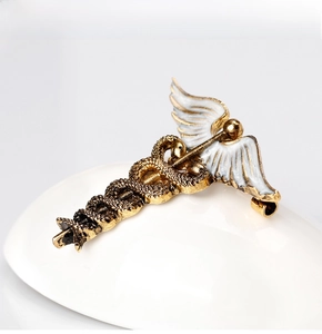 Detailed close-up of a vintage caduceus brooch with gold finish and white enamel wings
