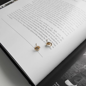 Detail view of gold star and moon stud earrings on an artistic book background