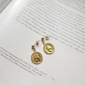 Close-up of gold 925 sterling silver coin earrings featuring relief on an open book