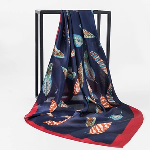 Detailed close-up of a floral silk scarf with vibrant feather prints and red border edges