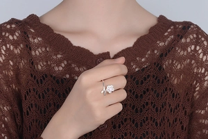Detail of adjustable silver flower ring with pink zircon on hand in brown knit sweater