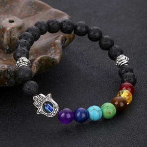 Chakra lava stone bracelet with Hamsa Hand and Evil Eye pendant on textured background