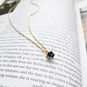 Detailed view of a gold necklace with a round sapphire pendant on an open book page