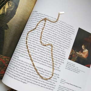 Detail of gold-plated irregular Figaro chain necklace resting on an open art book page