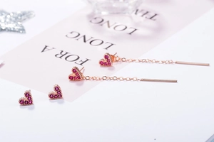 Macro shot of rose gold heart earrings and long chain studs with purple zircons