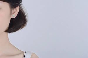 Close-up of heart-shaped earring with green cat-eye stone on a female model's ear