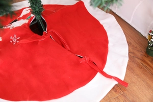 Detail of red Christmas tree skirt showing embroidery of snowflake and Santa Claus patterns