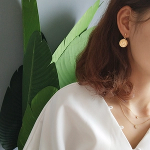 Detail view of a model wearing a gold coin stud earring and a layered star moon necklace