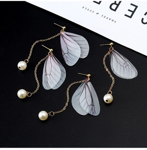 Detailed macro of vintage butterfly wing earrings with pearls on black and white surface