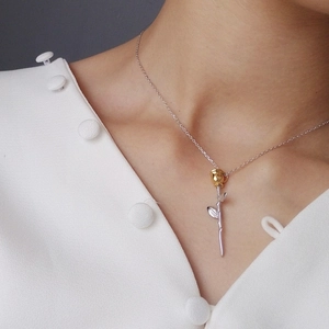 Detail of rose pendant necklace with gold petals and silver stem on a model
