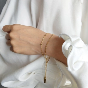 Close-up of golden double-layered bracelet with beads and rectangle charm on a wrist