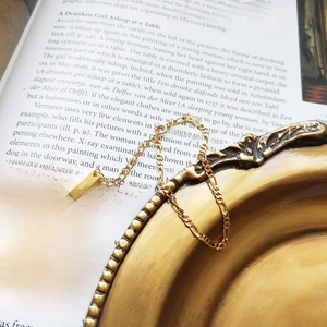 Detailed macro of golden Figaro chain bracelet with rectangular tag on vintage book