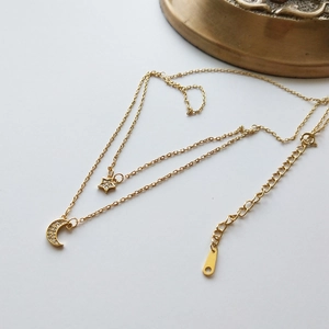 Detail of gold double-layer necklace with star and moon charms inlaid with zircons